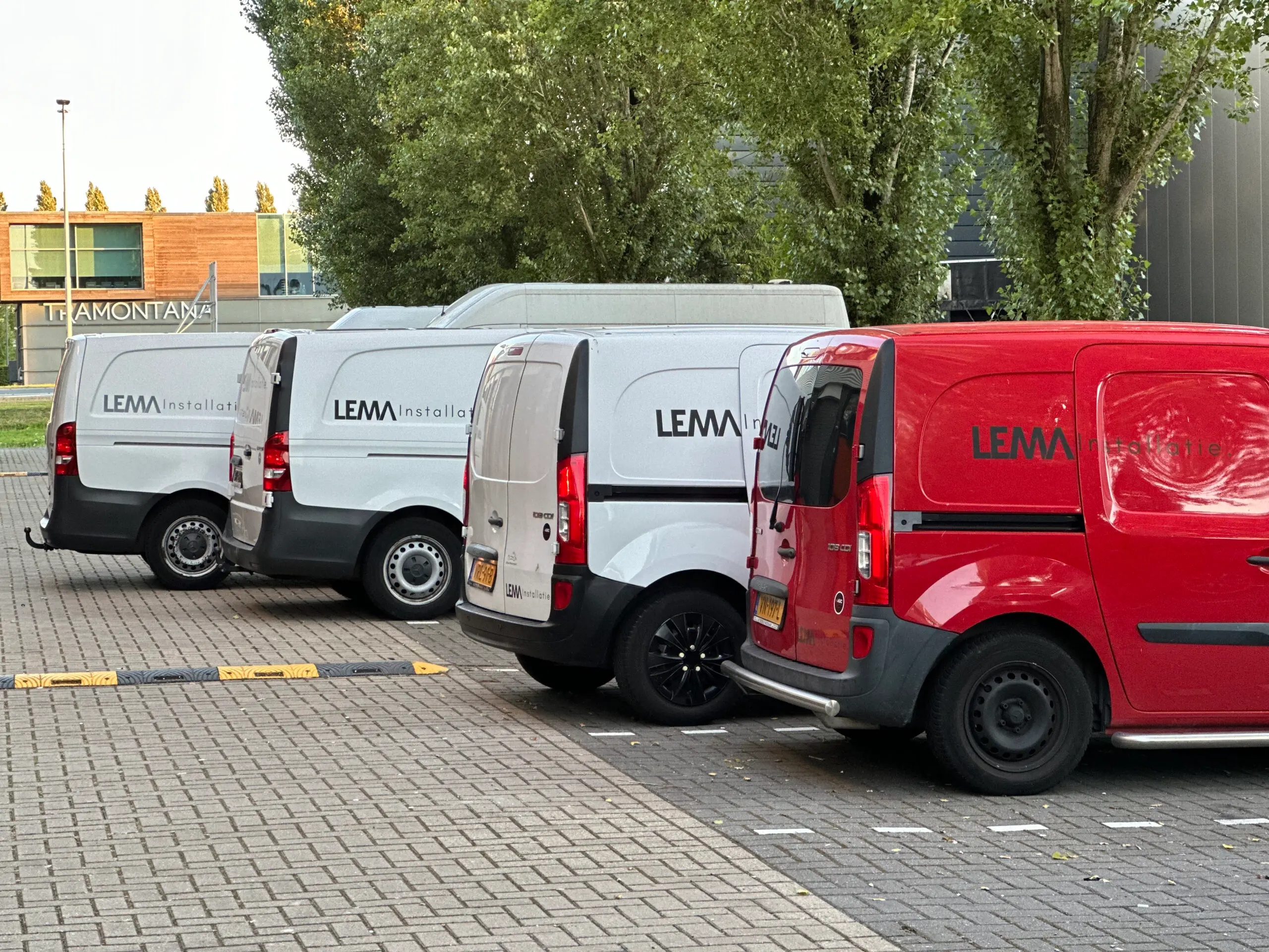 Vier bedrijfsbussen van LEMA Installatie op een rij, met het woordmerk op de zijkant; de rechter bus is rood.