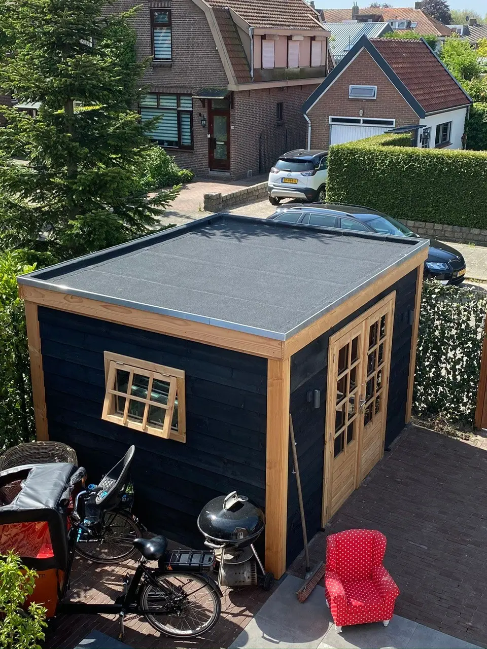 Zwart gebeitste tuinberging met een nieuw plat dak, bitumineuze dakbedekking en een verzinkte dakrand.